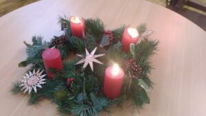 La couronne de l'avent disposé sur une table dans la salle de culte du temple. Trois bougies sur quatre sont allumées. La couronne est réalisée avec des branchage de sapin, des baies et des pommes de pins.