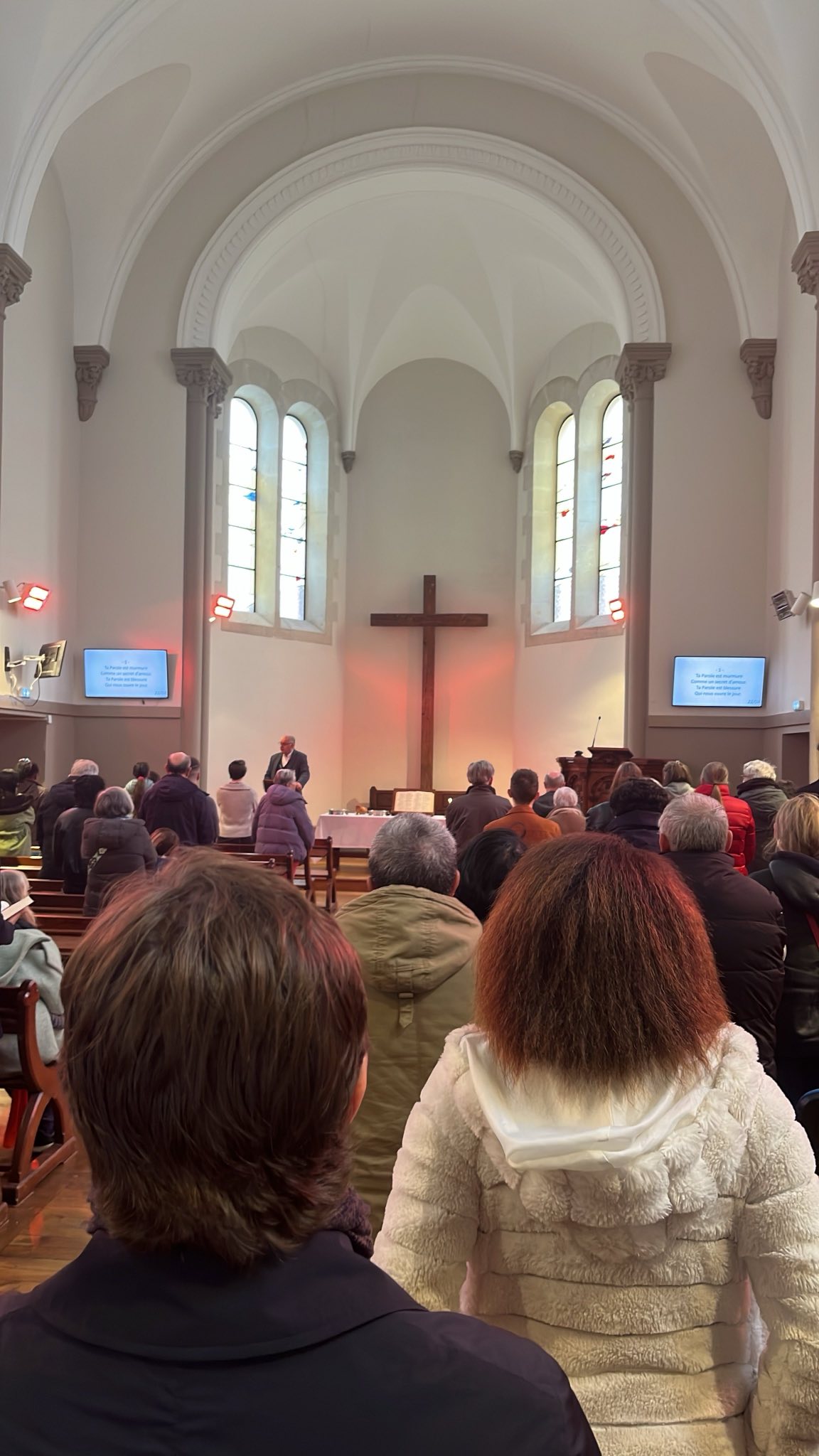 Photo prise du fond de la salle de culte. On y voit des paroissiens debout et le pasteur Hervé STÜCKER en train d eparler devant le pupitre.