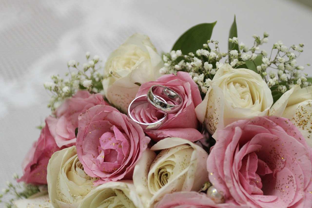 Un bouquet de roses de couleur blanches et roses avec deux alliances posés sur les fleurs.
