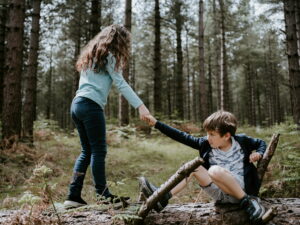 Une jeune fille qui aide un garçon à se relever après une chute en fôret.
