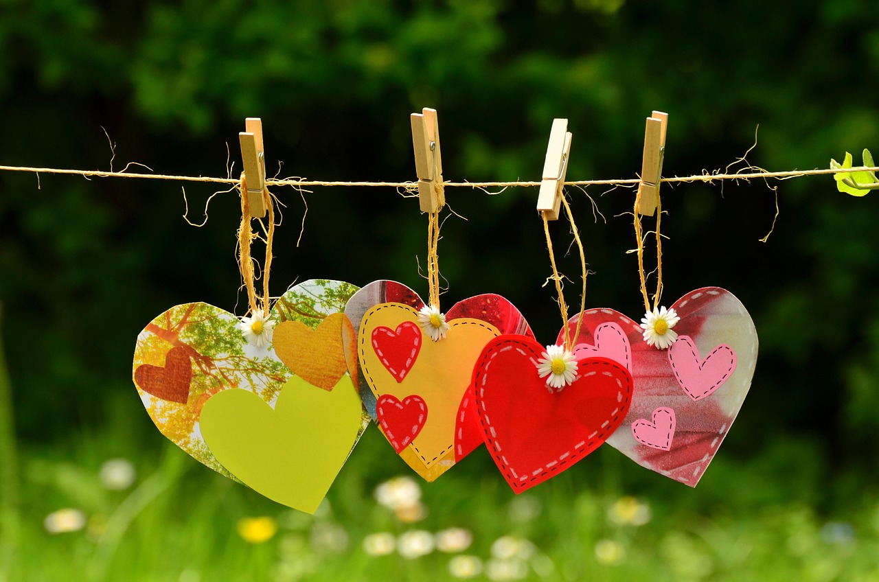 Quatre coeurs en cartons, joliment décoré accrochés à un fil grâce à des pinces à linge.