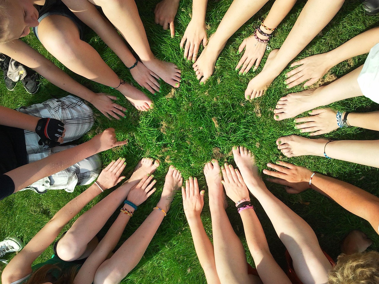 Un groupe de personnes assises en rond sur l'herbe. Des personnes, nous ne voyons que leurs jambes et leurs pieds nus.