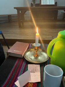 Une table dans la salle de culte avec une bougie allumée, un recueil de cantiques et une théiere.