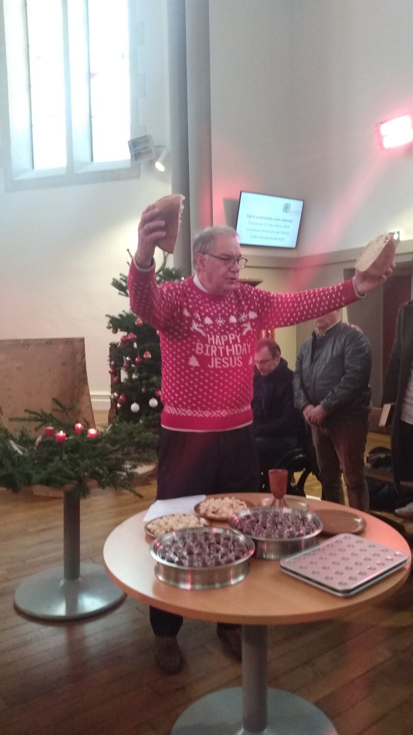 Le pasteur Hervé stûcker en train de célébrer la Sainte Céne avec un pull portant la mention Happy Birthday Jesus