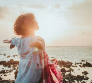 Une femme debout, les bras écartés devant la mer.