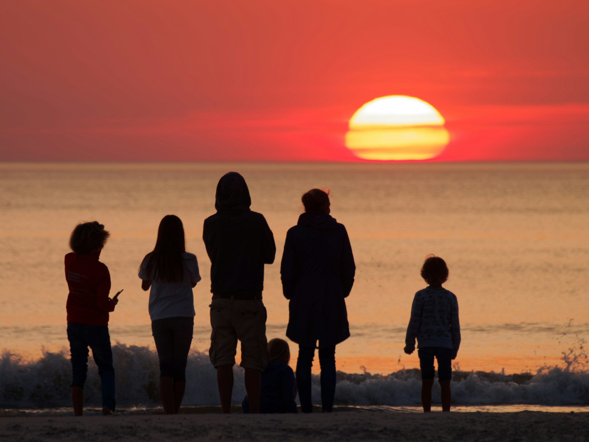 Deux adultes et quatres enfants devant un coucher de soleil sur la plage