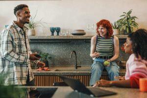 Trois amis en train de discuter dans une cuisine tout en grignotant.