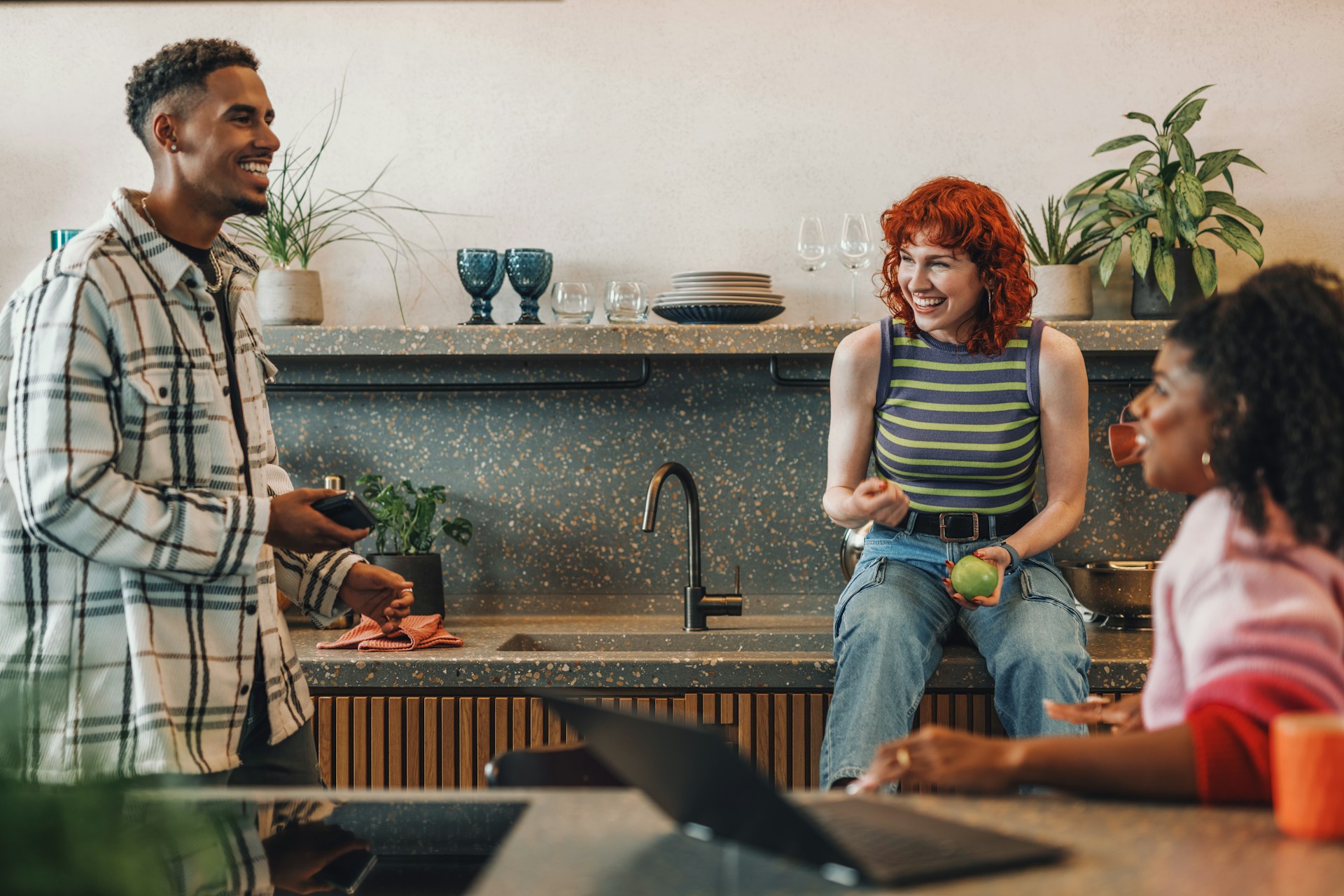 Trois amis en train de discuter dans une cuisine tout en grignotant.