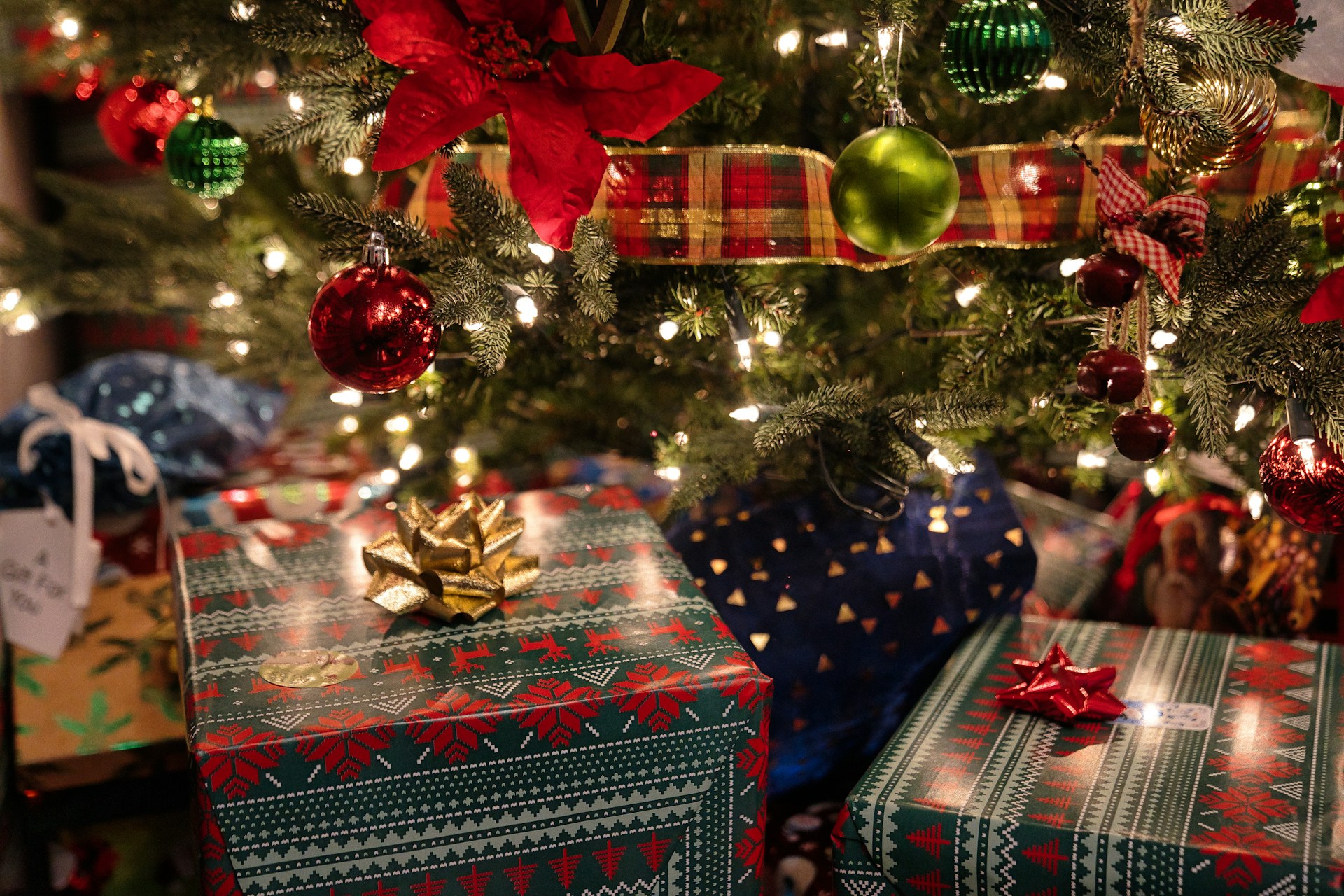 Des cadeaux emballés et déposés au pied d'un sapin décoré.